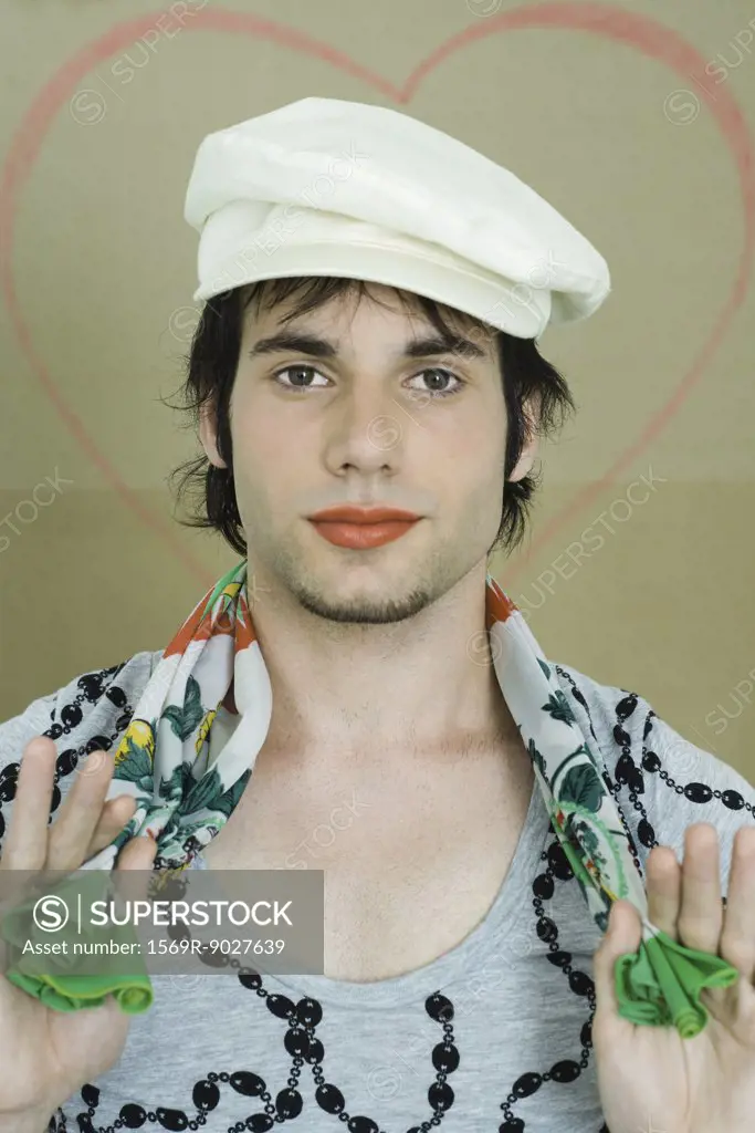 Young man wearing lipstick, cap, and scarf, smiling at camera, portrait
