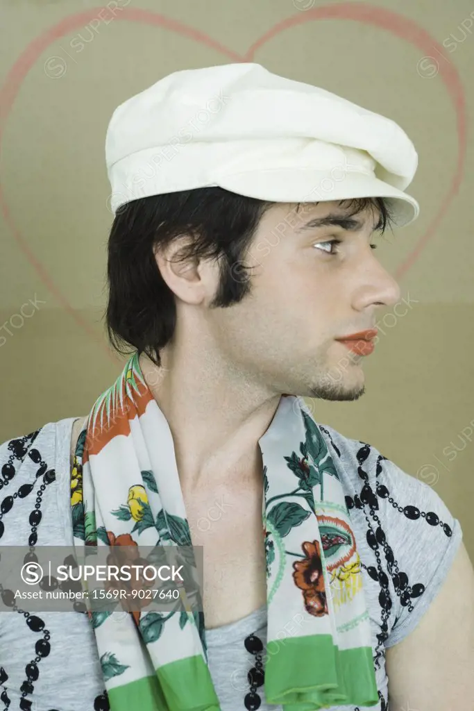 Young man wearing lipstick, cap, and scarf, looking away, portrait