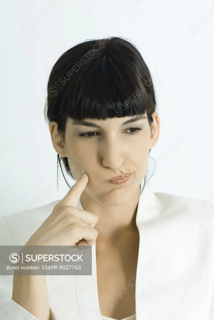 Young businesswoman puffing cheeks out, holding finger to cheek, looking away, portrait