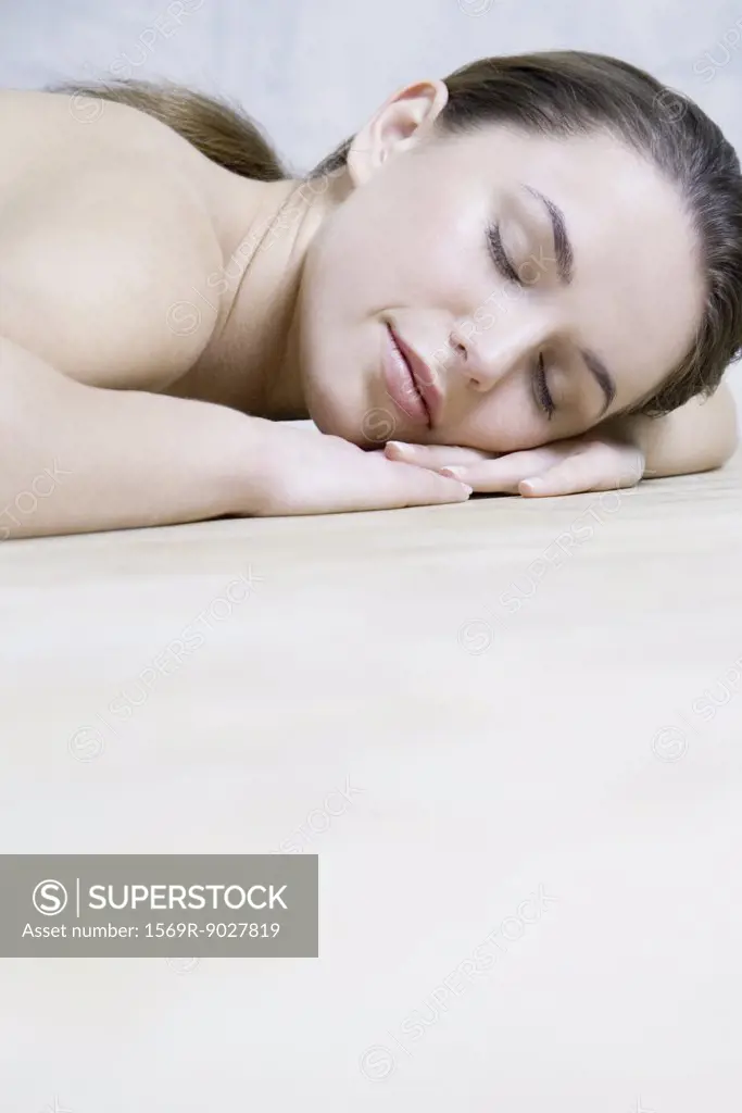 Young woman resting head on arms, eyes closed, cropped view