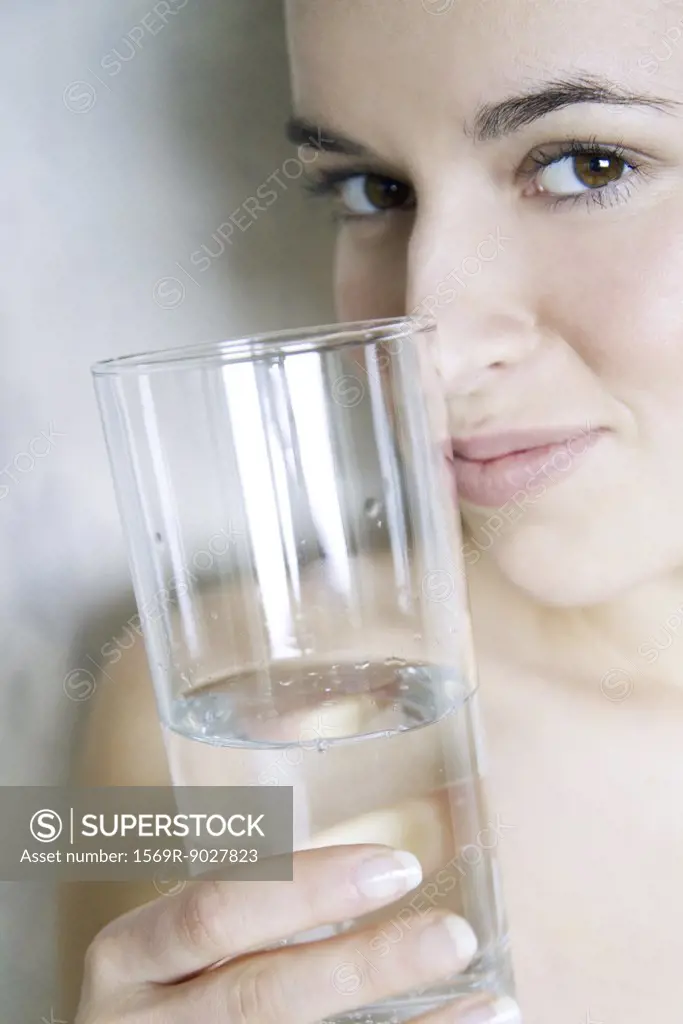 Young woman holding glass of water, smiling at camera, cropped view