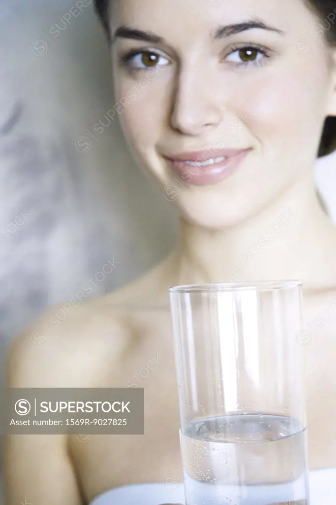 Young woman holding glass of water, smiling at camera