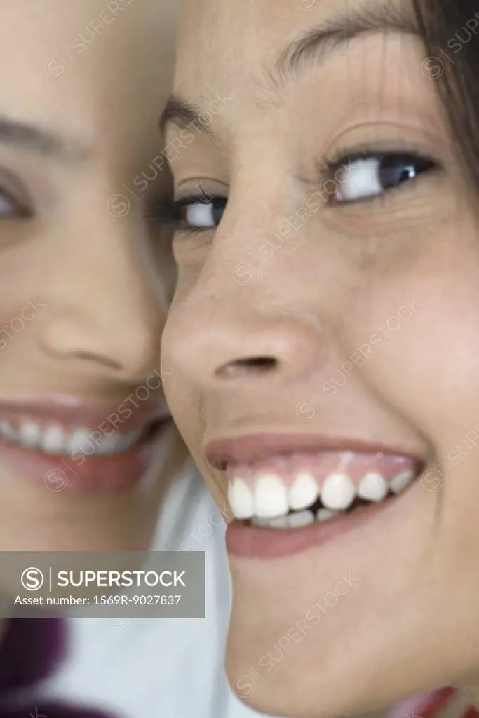Two young female friends smiling at camera, extreme close-up of faces, cropped