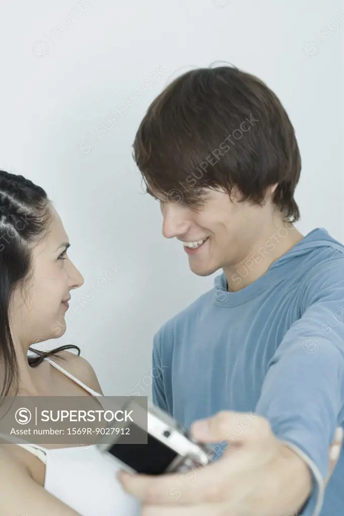 Young couple smiling at each other, man taking photo with digital camera