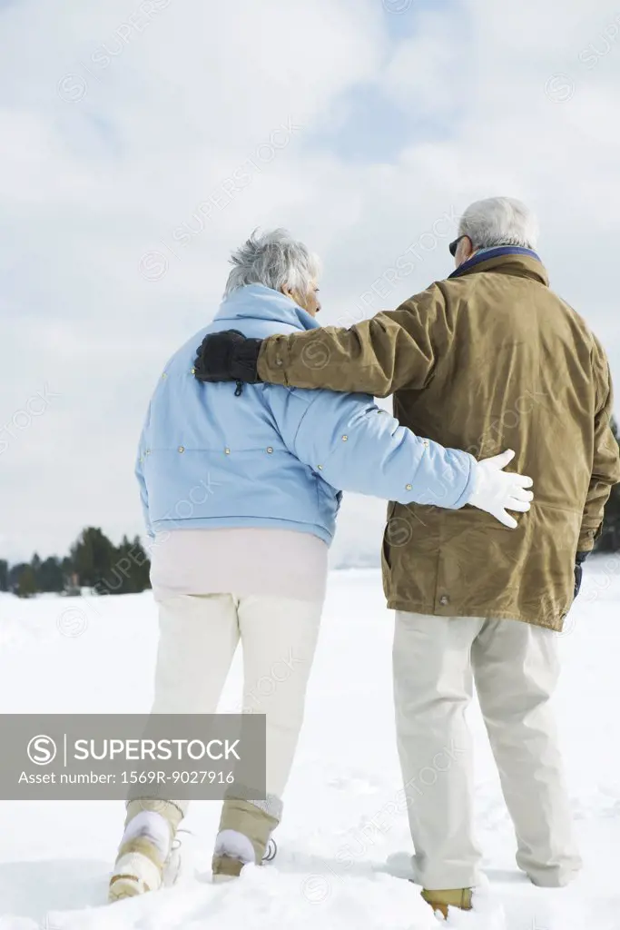 Senior couple walking together in snow, full length, rear view