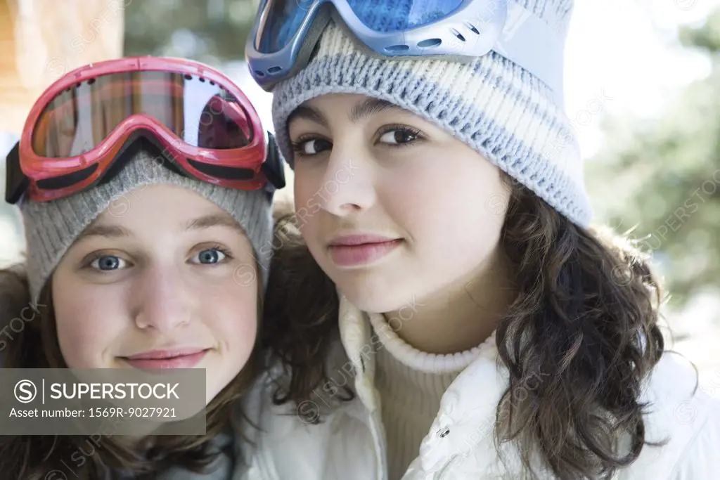 Two young friends wearing knit hats and ski goggles, smiling at camera, portrait