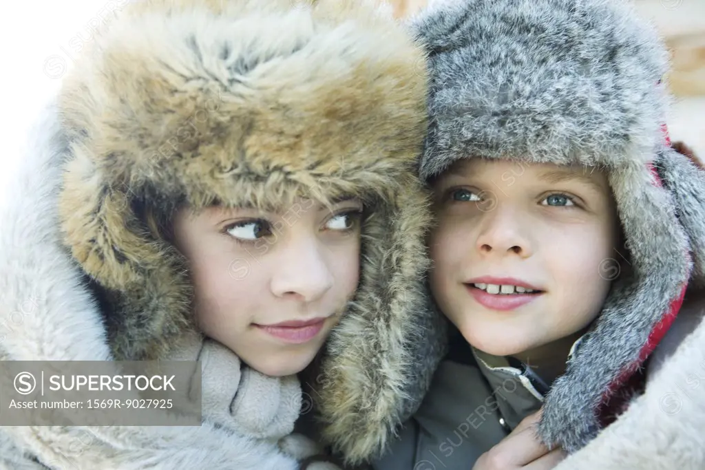 Sister and brother wearing fur caps, smiling, looking away, portrait