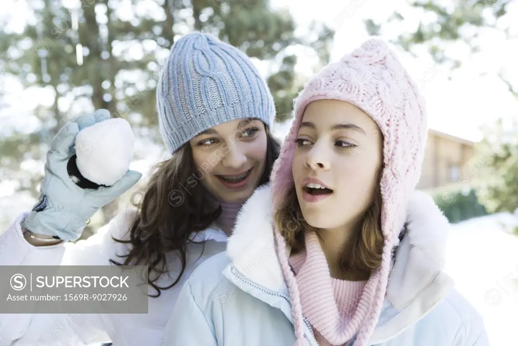 Teenage girl standing behind friend, holding up snowball, smiling