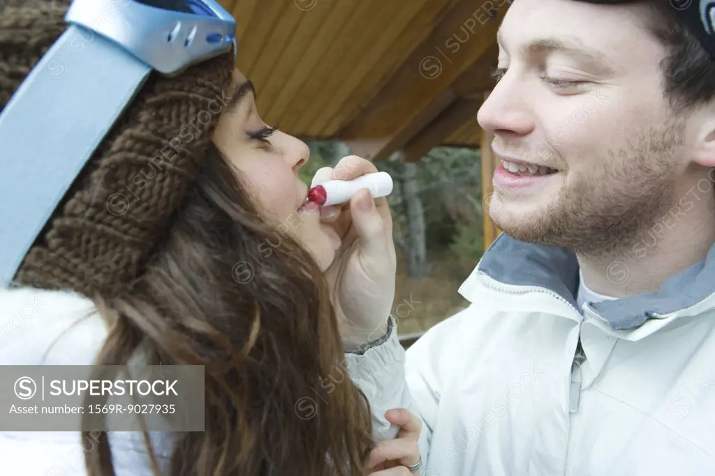 Young man applying lipstick to girlfriend's lips, side view