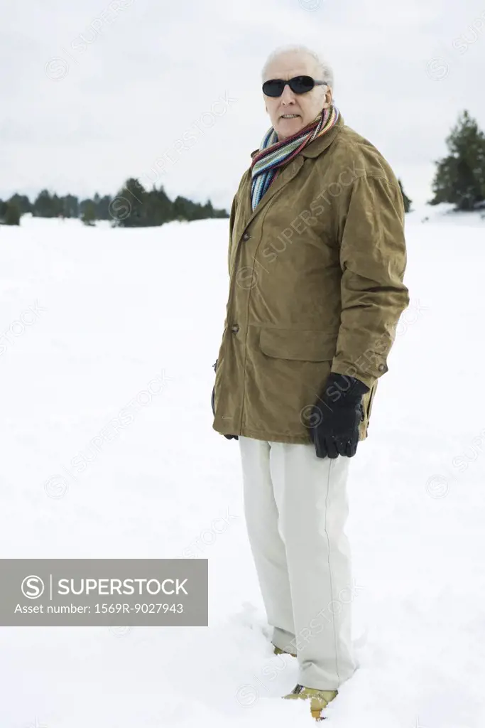 Senior man standing in snow, looking at camera, portrait