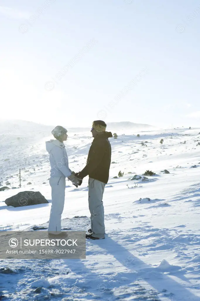 Male and female standing in snow, holding hands, face to face, full length