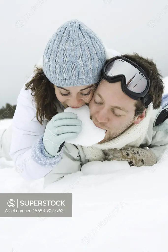 Young couple lying on the ground, eating snow together,  eyes closed