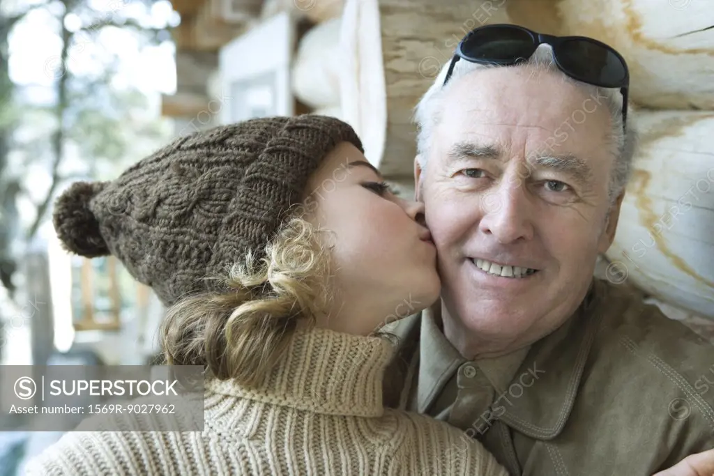 Senior man smiling at camera, granddaughter kissing him on the cheek, portrait
