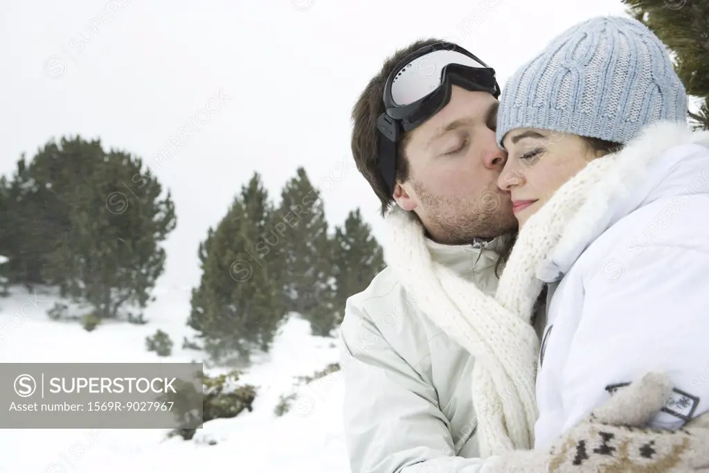 Young man kissing girlfriend, both with eyes closed, portrait
