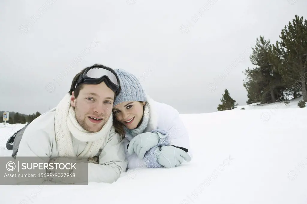 Young couple lying side by side in snow, smiling at camera, portrait