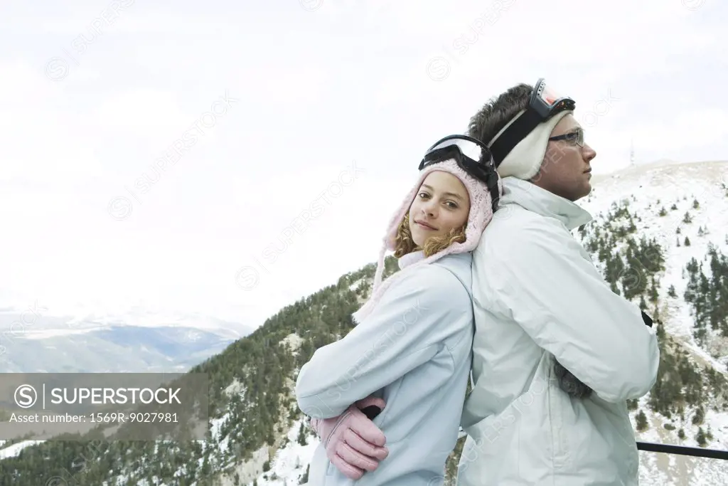 Two young skiers standing back to back, smiling, one looking at camera, portrait