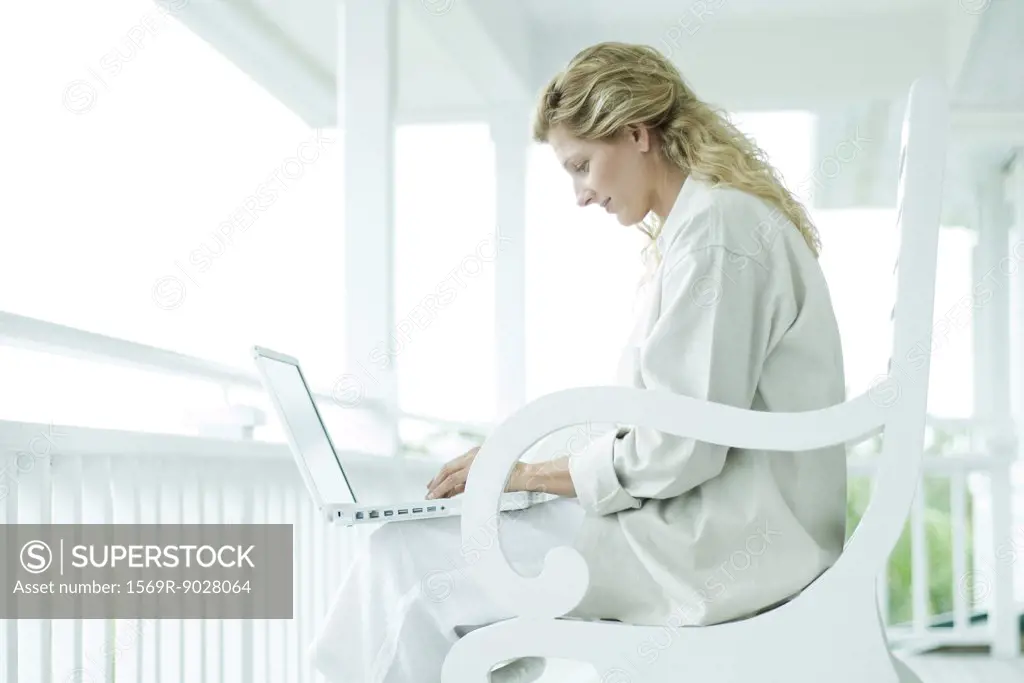 Woman sitting on porch, using laptop computer, smiling