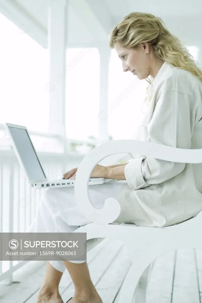 Woman sitting on porch, using laptop computer, side view