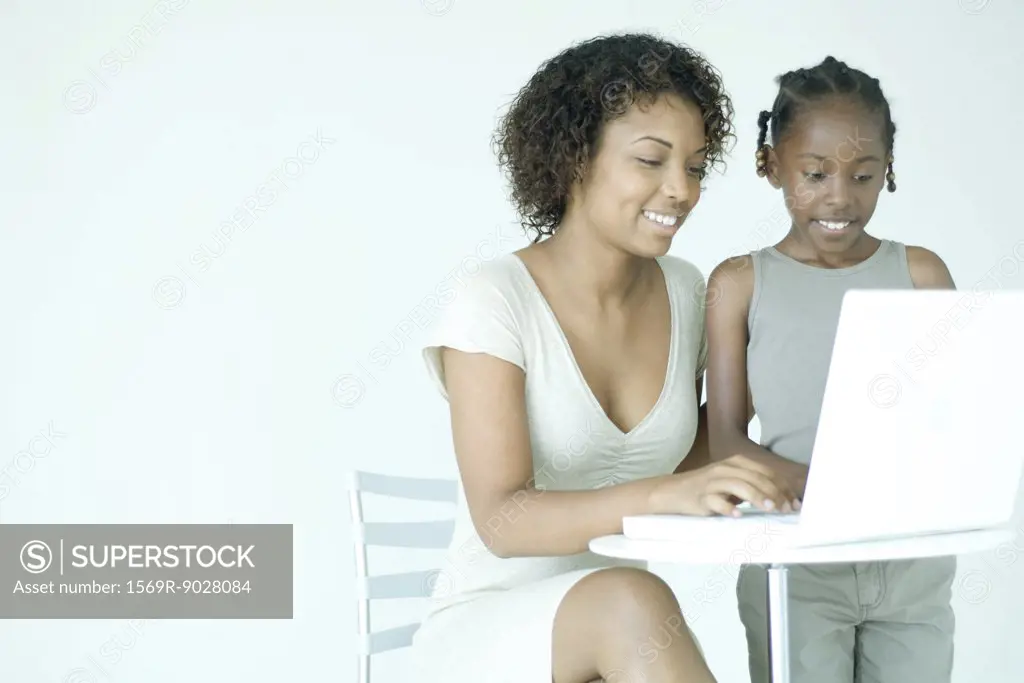 Mother and daughter using laptop computer together, smiling, looking down