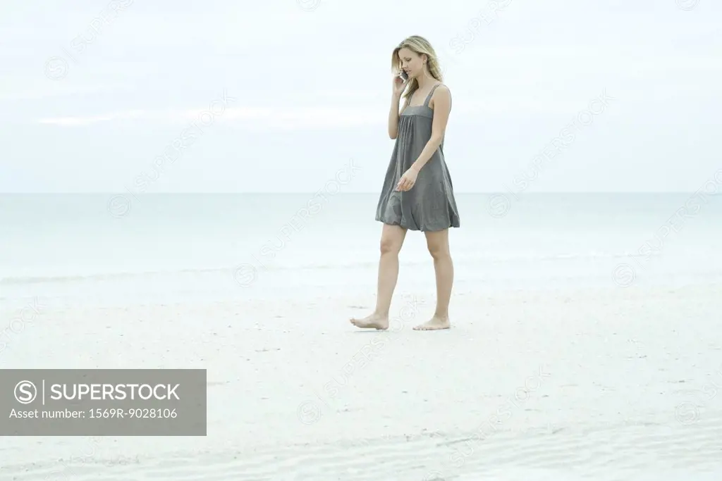 Young woman walking on beach, using cell phone, looking down