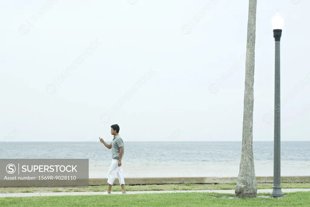 Man walking on sidewalk at the beach, looking at cell phone