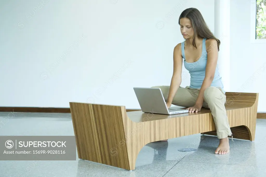 Teen girl sitting on bench, using laptop computer, looking down