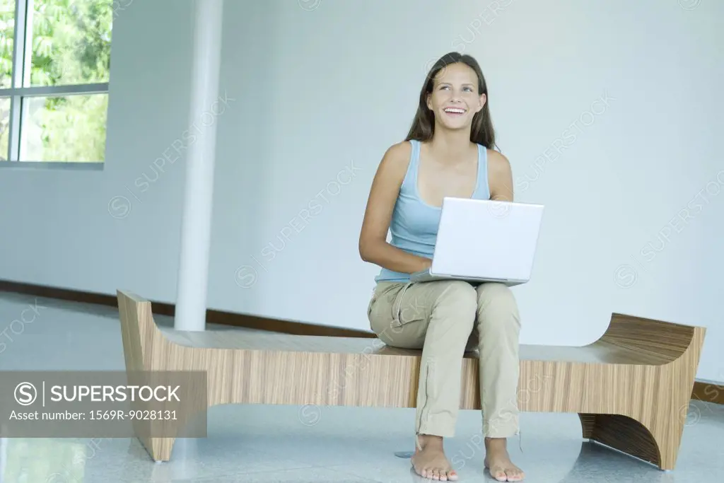 Teen girl sitting on bench, using laptop computer, smiling, looking up