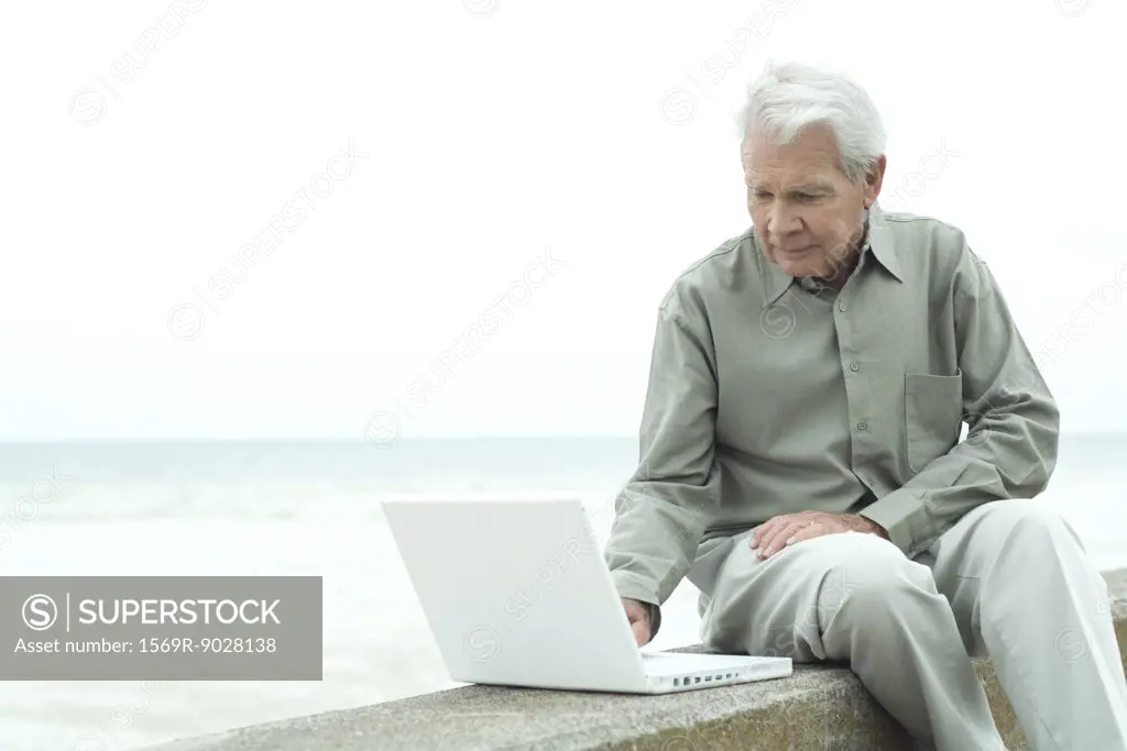 Senior man sitting outdoors using laptop computer, looking down