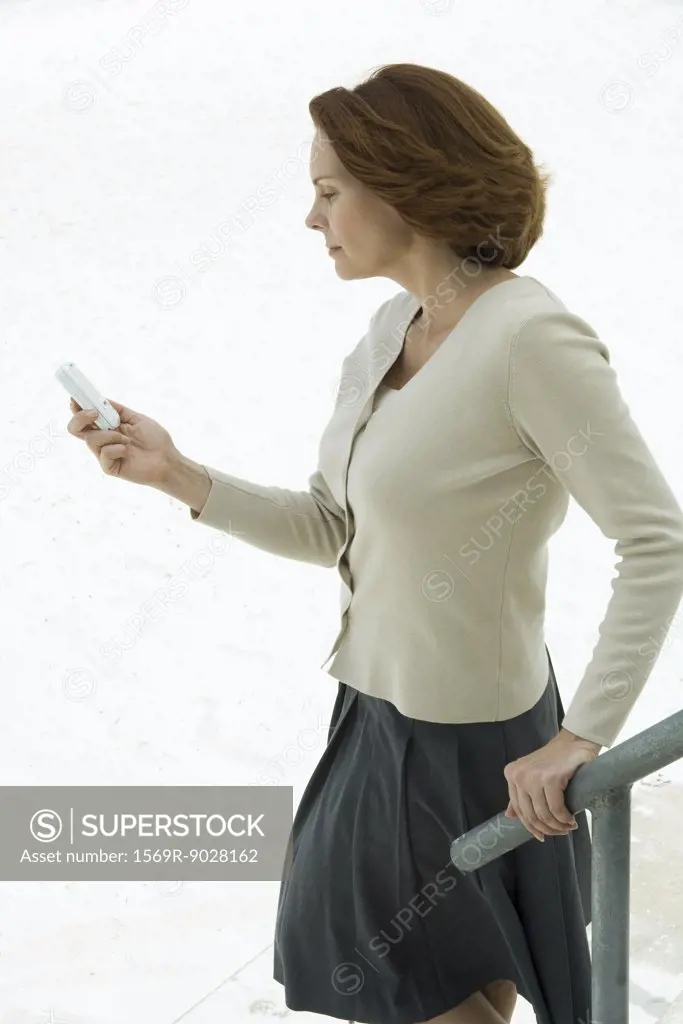 Woman holding railing, looking down at cell phone