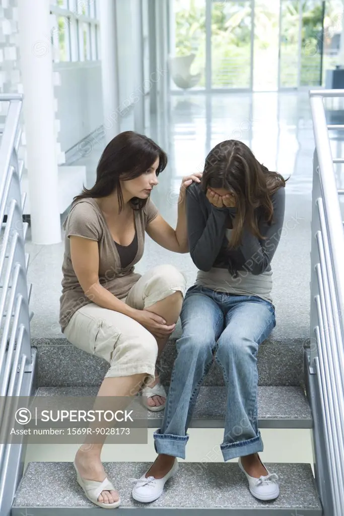Mother comforting teenage daughter, sitting on steps