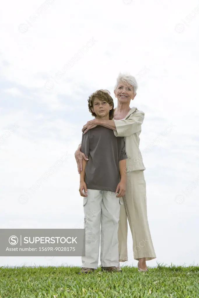 Senior woman and grandson, standing on grass, full length