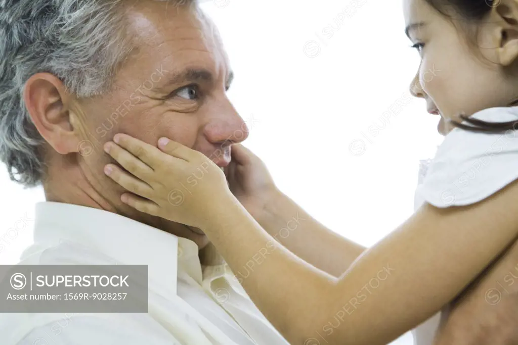 Man holding up little girl, girl's hands on man's cheeks, close-up