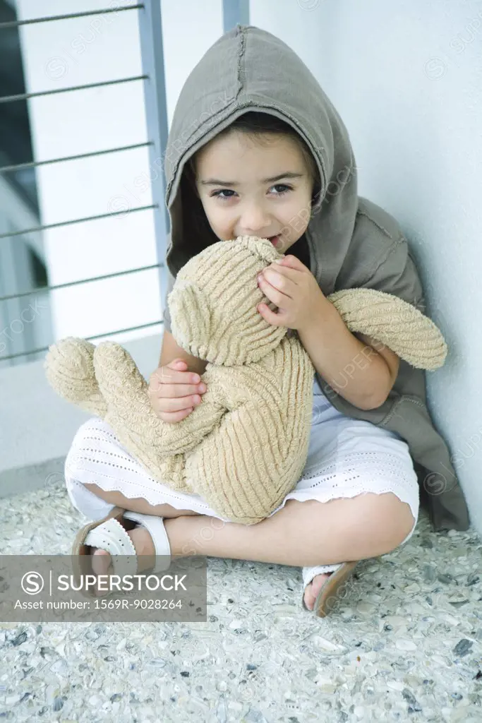 Little girl sitting on floor, whispering into teddy bear's ear, full length