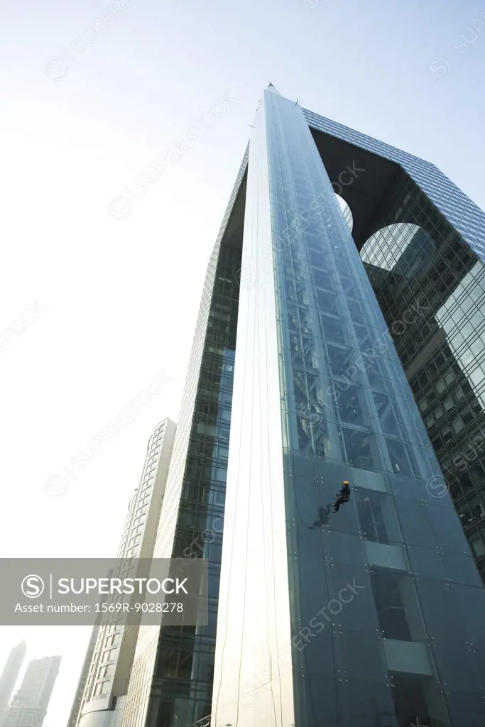 Window washer on side of skyscraper, low angle view