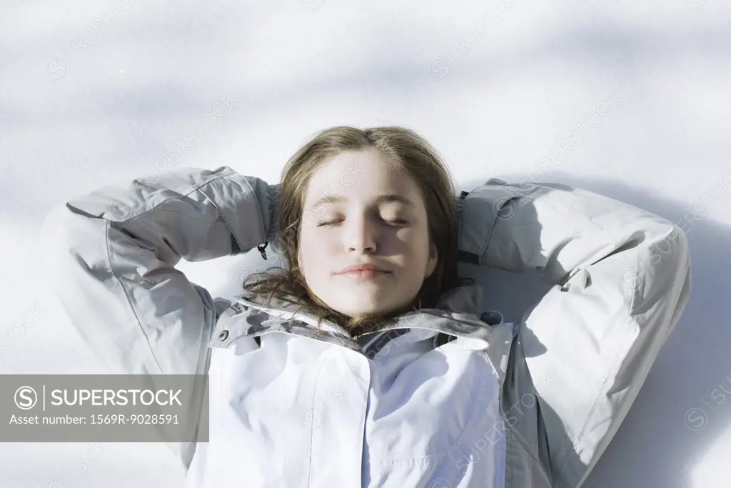 Teenage girl lying on snow with hands behind head and eyes closed