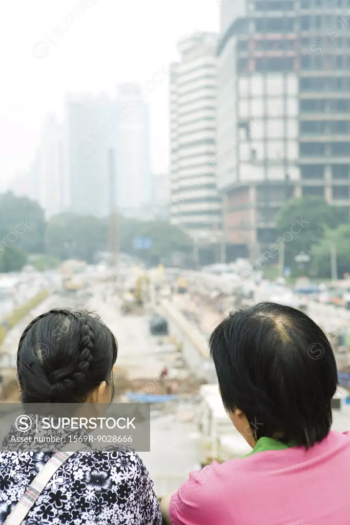 China, Guangdong Province, Guangzhou, two people looking out over construction site, rear view, close-up