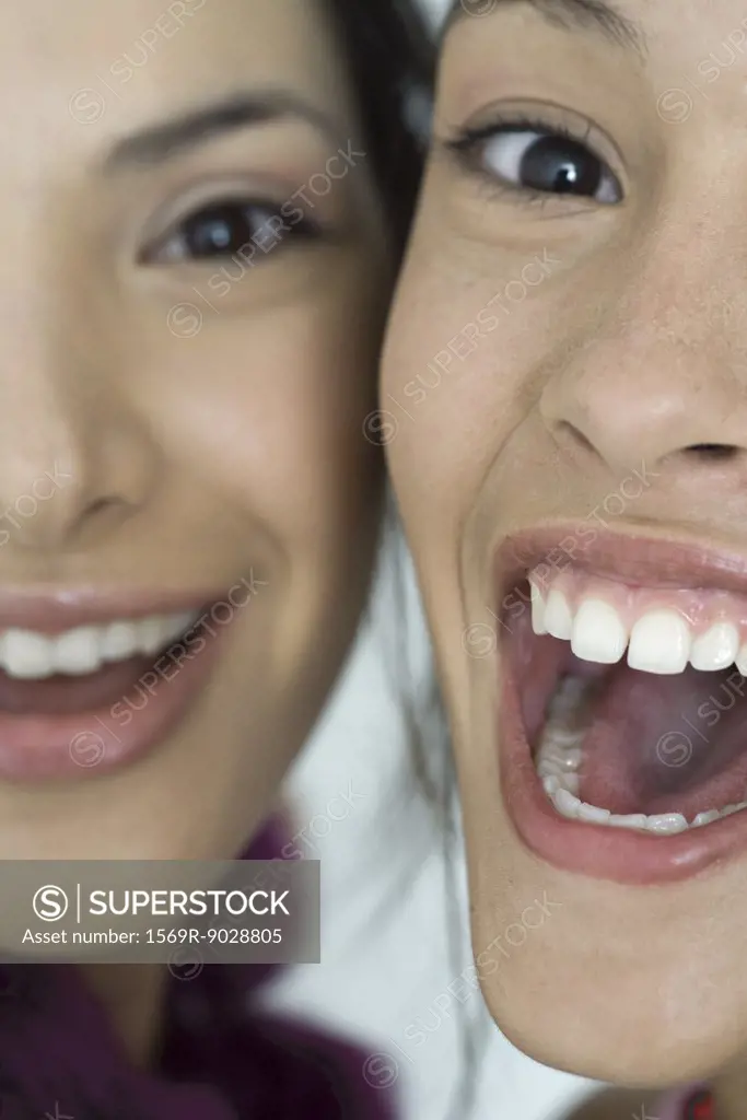 Two young female friends smiling with mouths wide open, looking at camera, extreme close-up of faces, cropped