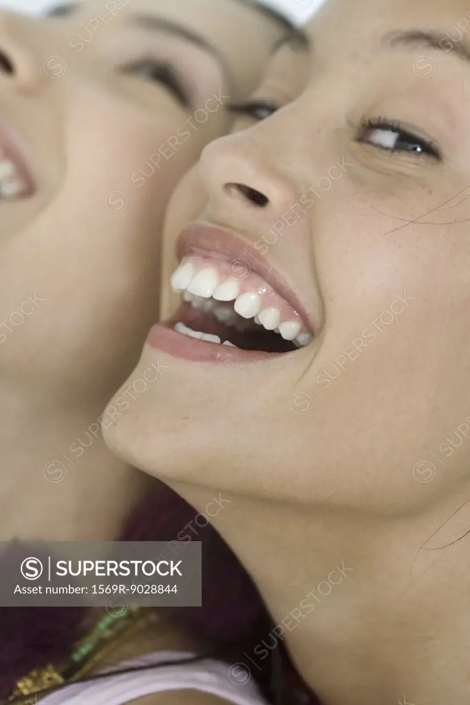 Two young female friends laughing, one looking at camera, extreme close-up of faces, cropped