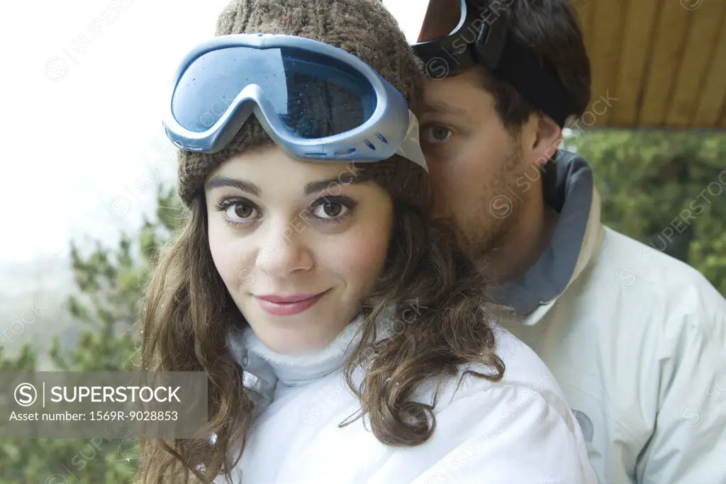 Young couple standing together, female smiling at camera, boyfriend peeking from behind