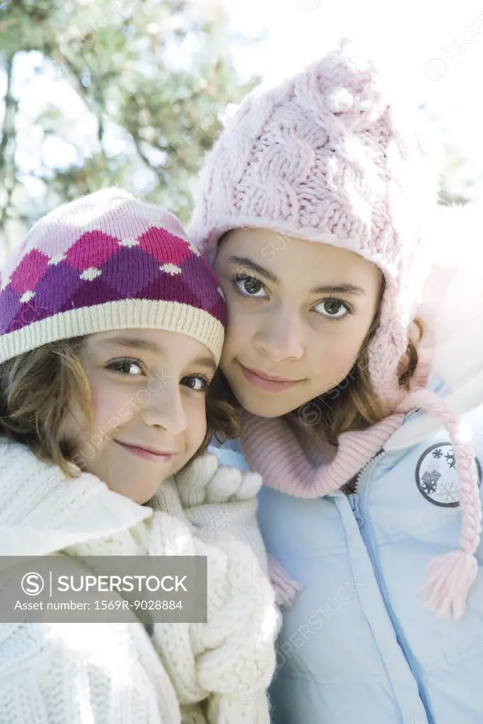 Two sisters smiling at camera, cheek to cheek, both wearing knit hats, portrait