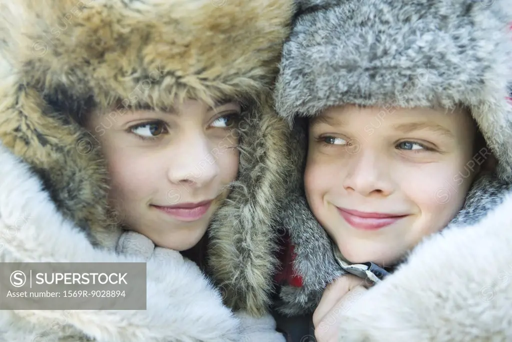 Sister and brother wearing fur caps, smiling, looking away, portrait