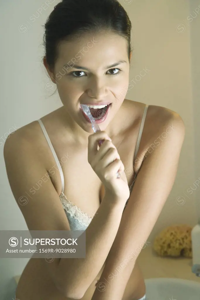 Young woman in underclothes brushing teeth, looking at camera