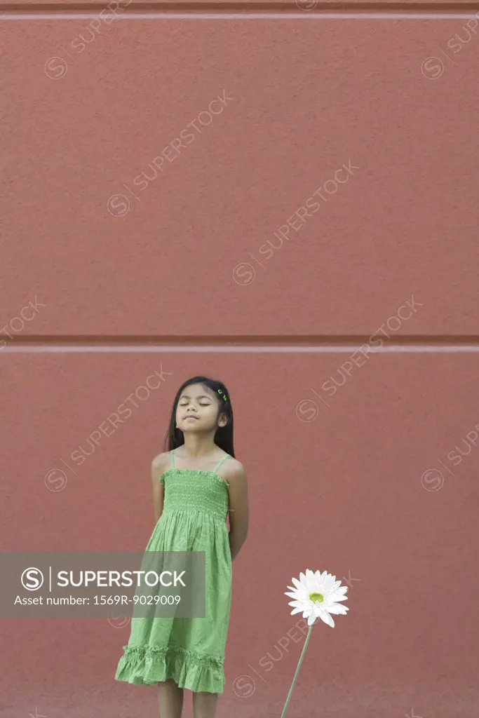 Girl standing with eyes closed and hands behind back, next to flower