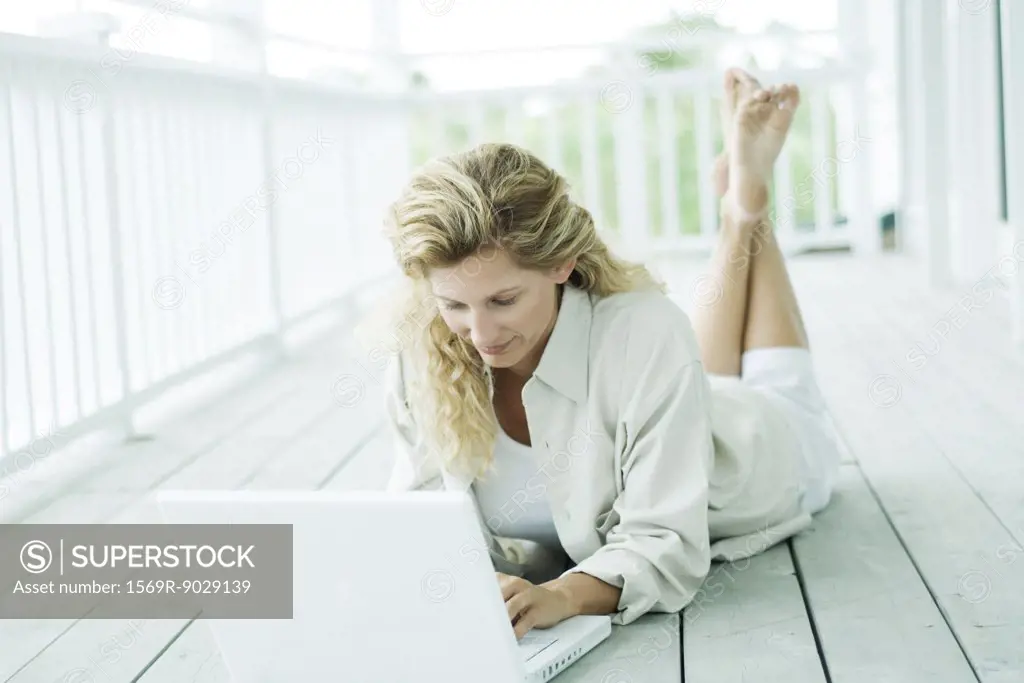 Woman lying on stomach on deck, using laptop, looking down