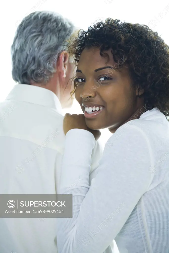 Young woman with hand on mature man's shoulder, smiling over shoulder at camera