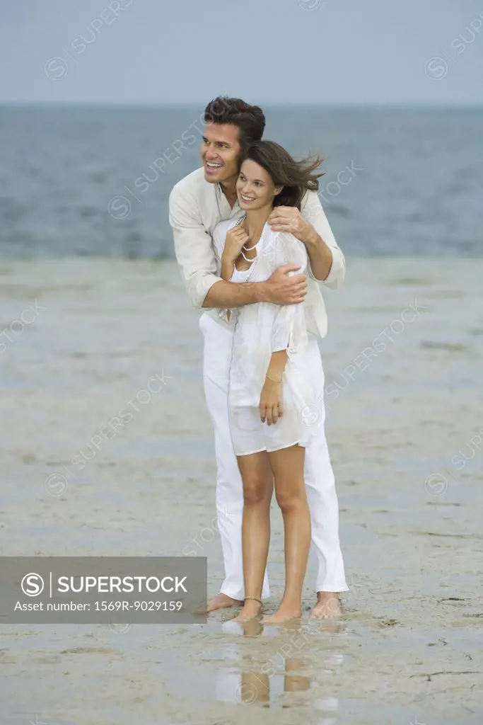 Man and teen girl on beach, standing together, looking at view, full length