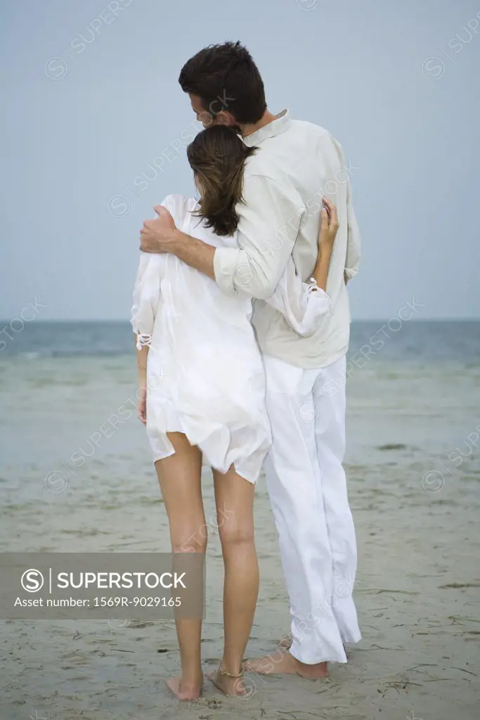 Man and teenage girl on beach, standing together, looking at view, full length, rear view