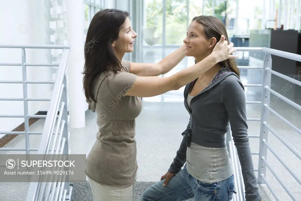 Mother and teenage girl together, woman pushing daughter's hair back, side view