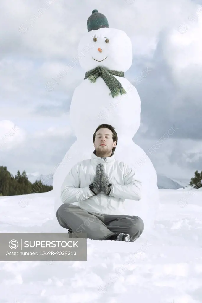 Young man meditating in front of snowman
