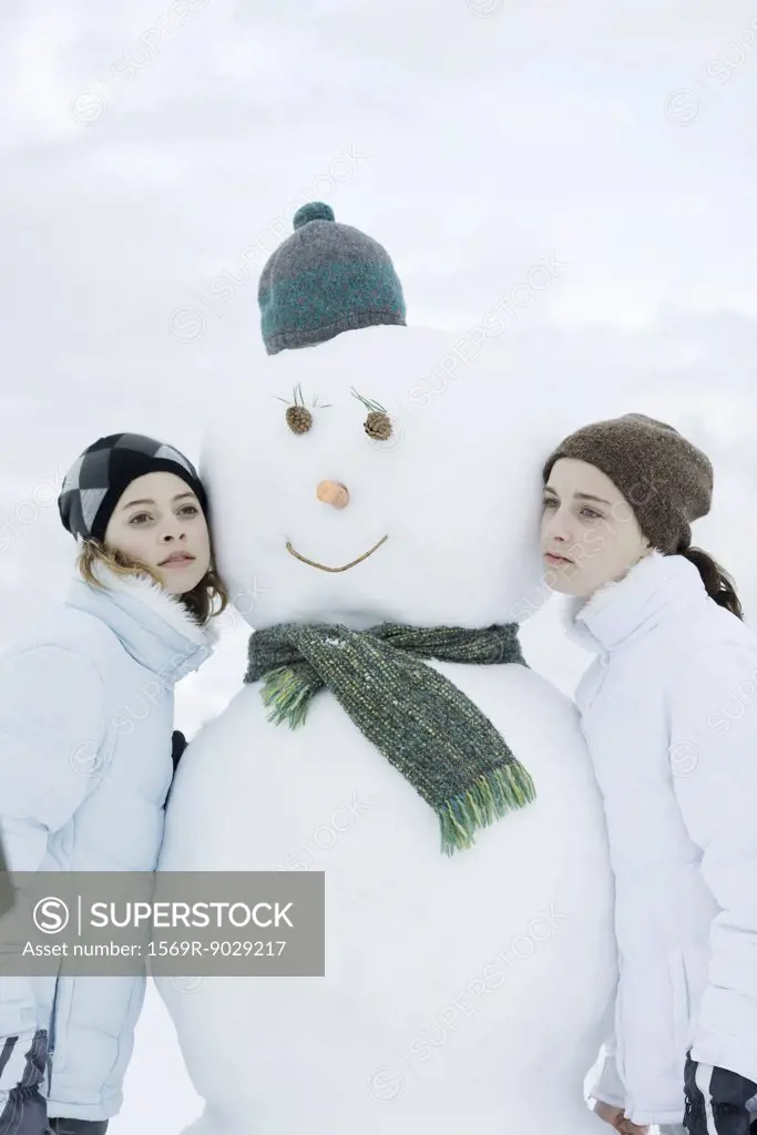 Two teen girls leaning against snowman
